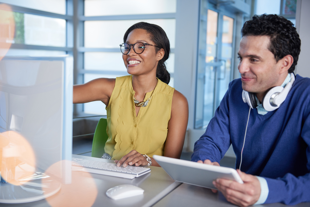 Two colleages discussing ideas using a tablet and computer
